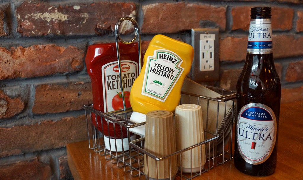 Un présentoir de condiments — ketchup, moutarde et bière — sur une table de diner américain.