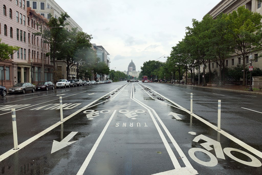 Une avenue humide de pluie mène vers le Capitole, marquages au sol pour vélos et virages.