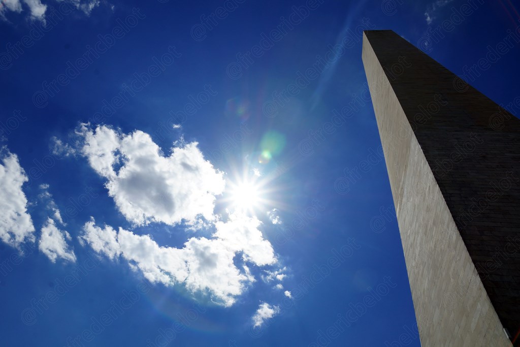 Vue en contre-plongée sur l'obélisque du Washington Monument, soleil éclatant derrière.