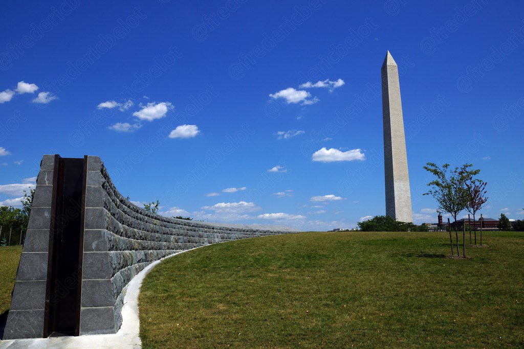 Le Washington Monument vu depuis un mur courbe en granit, pelouse dégagée alentour.