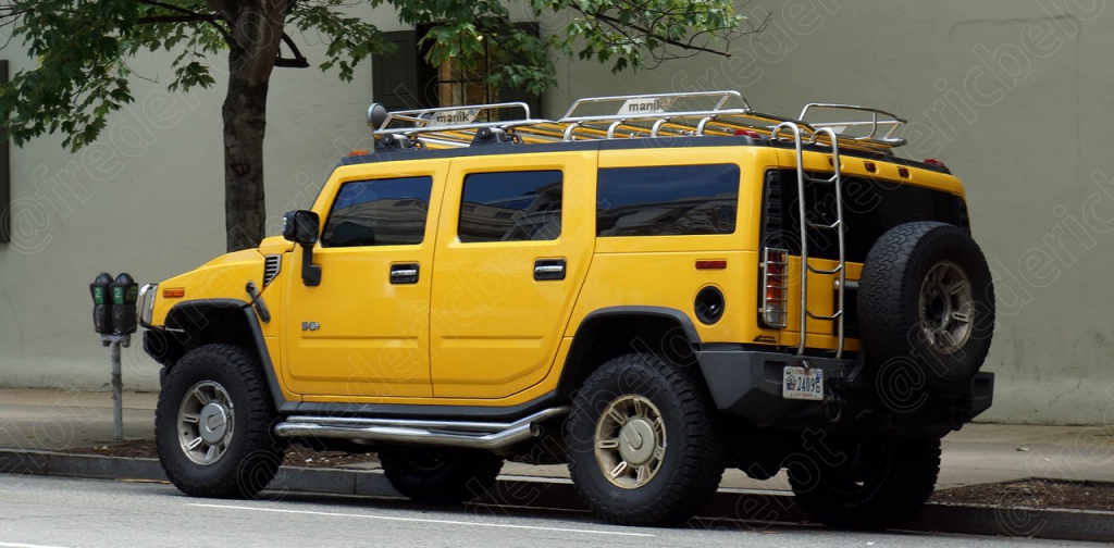 Un Hummer H2 jaune garé dans une rue résidentielle ombragée.