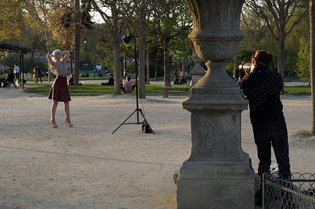 Un photographe et son assistant installent un éclairage de studio en extérieur pour une séance photo dans un parc parisien.