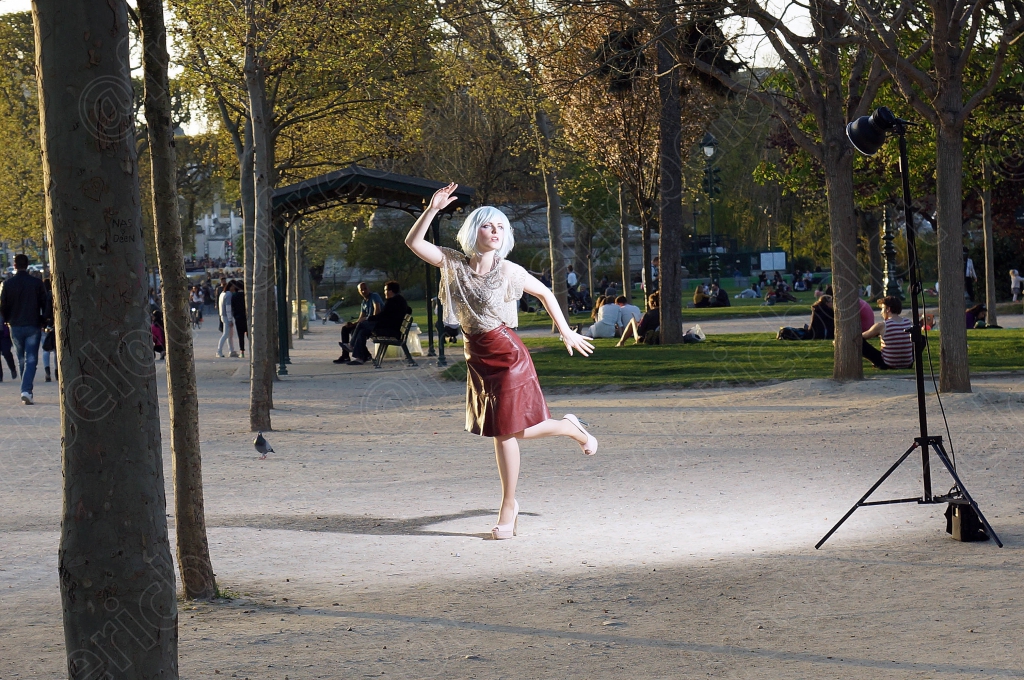 La même jeune femme pose en mouvement, bras levé, éclairée par un flash de studio sous les arbres.