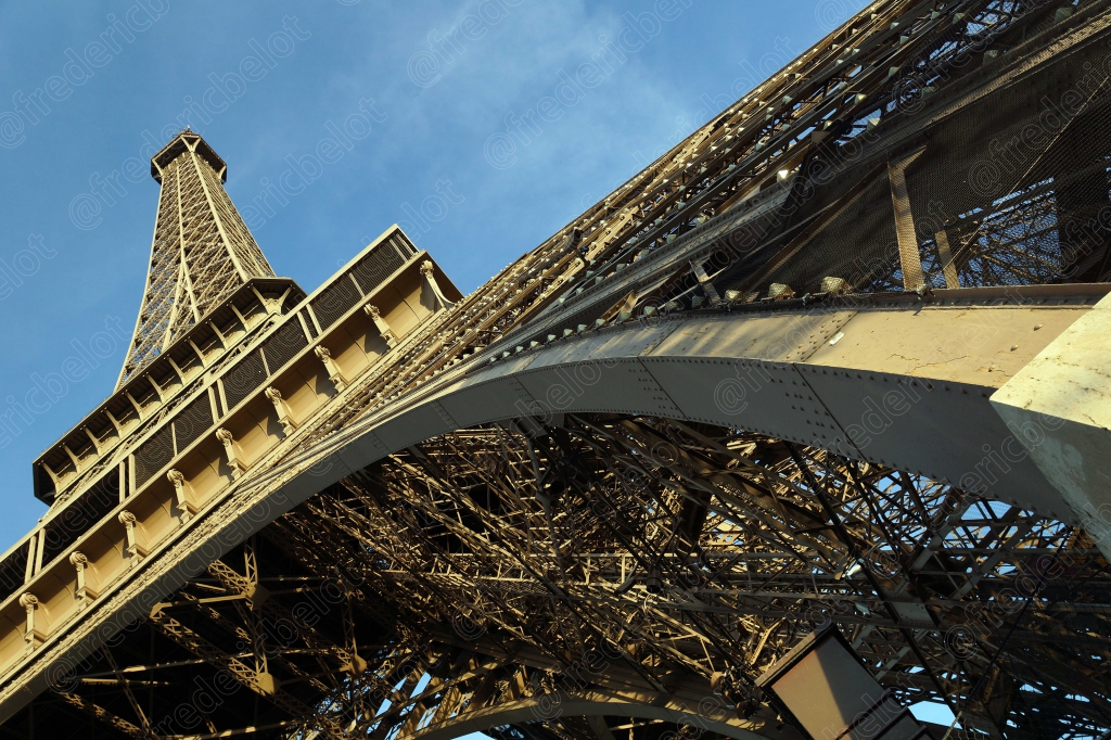 Vue en contre-plongée sur la structure métallique et les arches de la tour Eiffel.