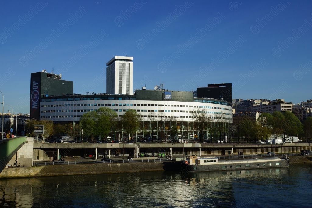 Un immeuble moderne aux lignes courbes en bord de Seine, sous un ciel bleu clair.