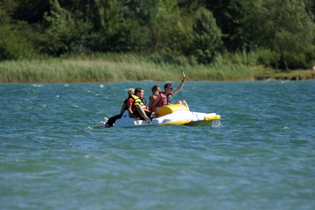 Une famille s'amuse sur un jouet gonflable flottant, saluant depuis l'eau du lac.