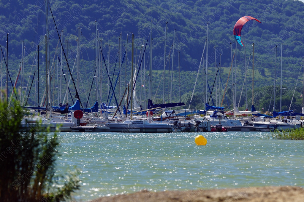 Un port de plaisance avec ses voiliers amarrés, un kitesurfeur passant au loin.