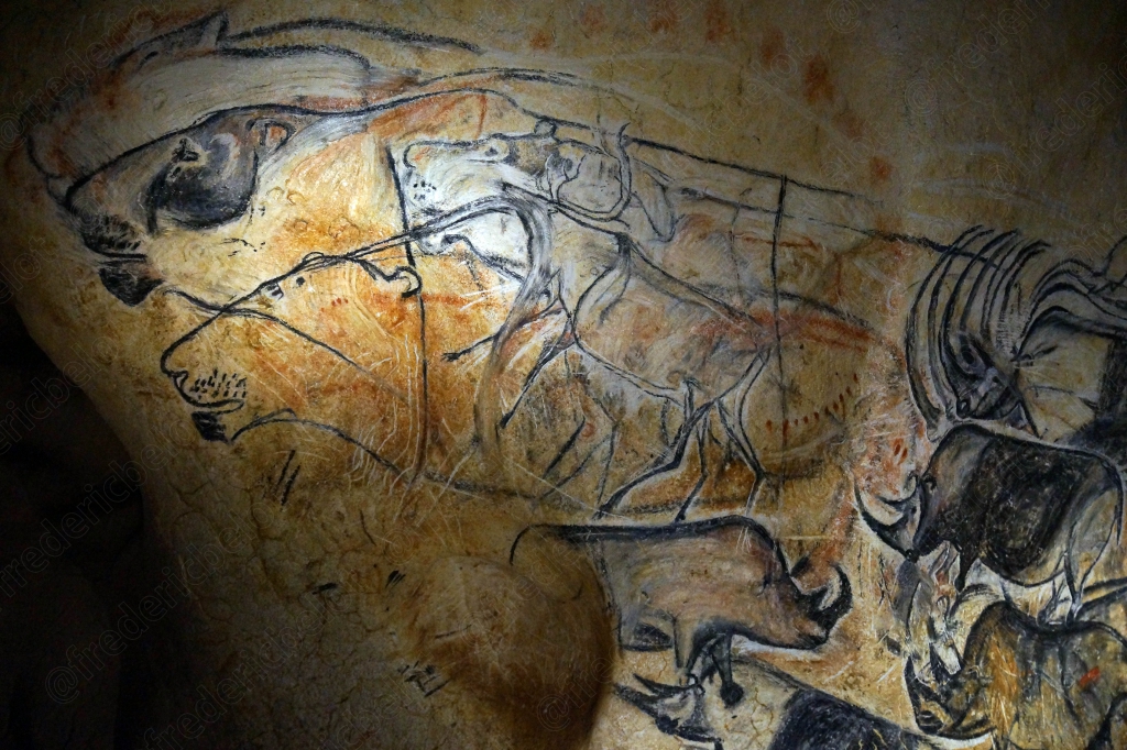 Chevaux et bisons dessinés au trait noir se chevauchent sur la roche, éclairés en contre-jour.