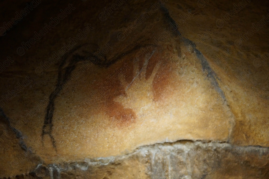 Une main négative rouge apposée sur la roche, entourée de traces ocre.