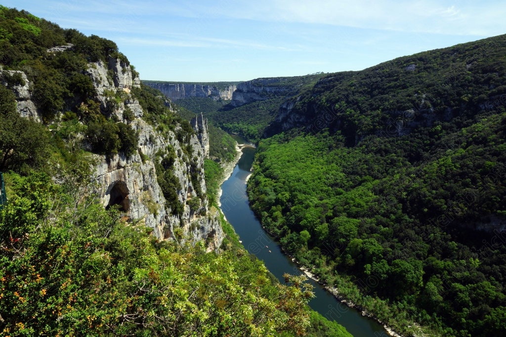 Une grotte visible à flanc de falaise surplombe la rivière qui serpente entre les gorges.