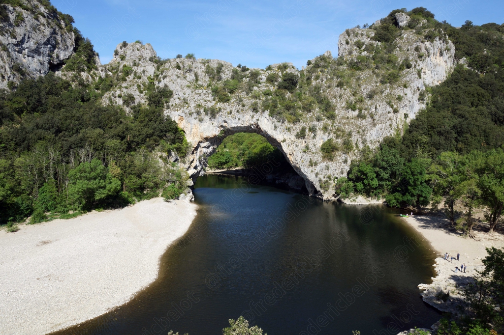 Le Pont d'Arc, arche naturelle de pierre, enjambe la rivière bordée de plages de galets.