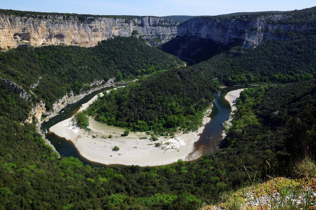 Un large méandre de la rivière encercle presque totalement un banc de galets blancs.