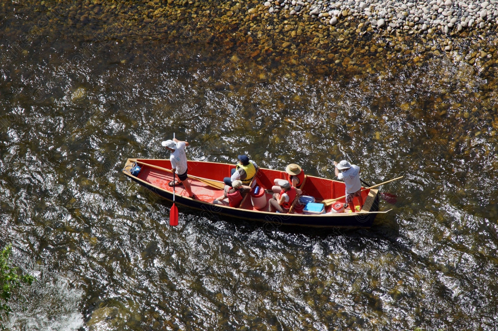 Un bateau à rames rouge transporte plusieurs passagers sur les eaux calmes de la rivière, vu de haut.