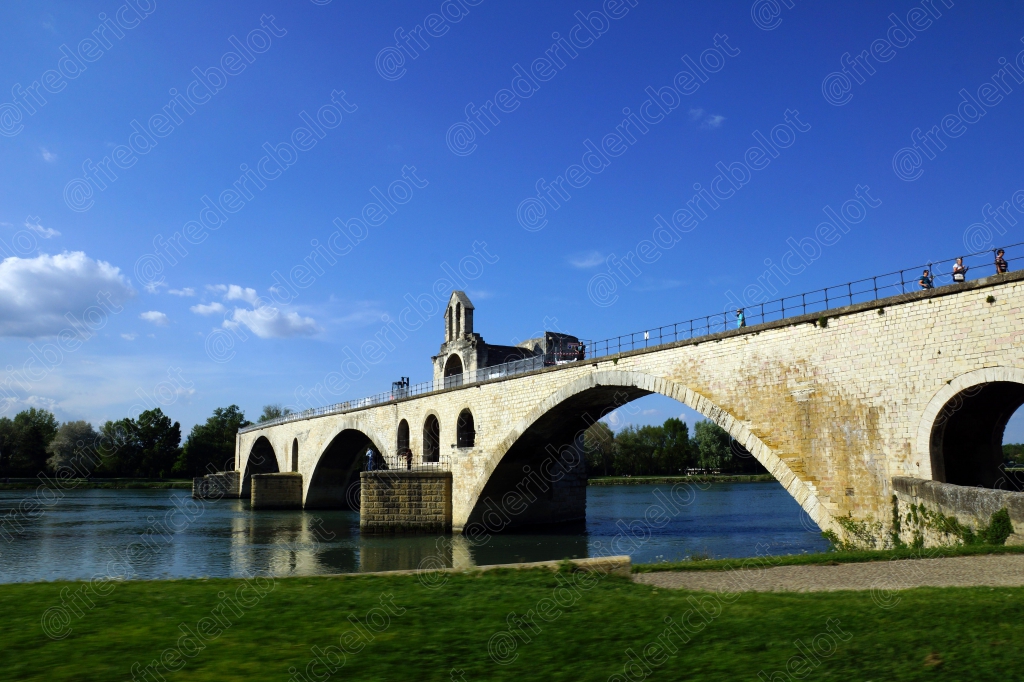 Le pont d'Avignon vu au ras de l'eau, ses arches de pierre se détachant sur un ciel bleu.
