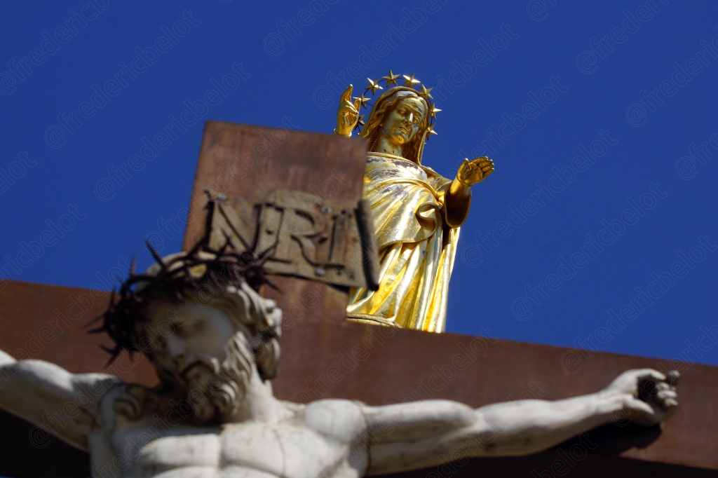 Un christ en croix doré surmonté de rayons, sur fond de ciel bleu.