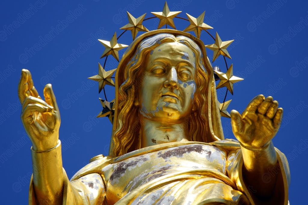 Une statue dorée de la Vierge, auréolée d'étoiles, bras ouverts vers le ciel.