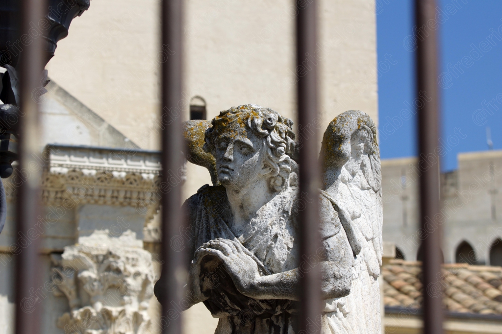 Des statues aperçues à travers une grille en fer forgé, devant une façade ancienne.