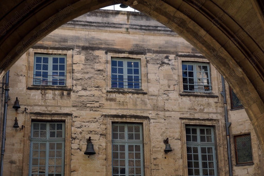 Une façade avignonnaise classique vue sous une arche de pierre.
