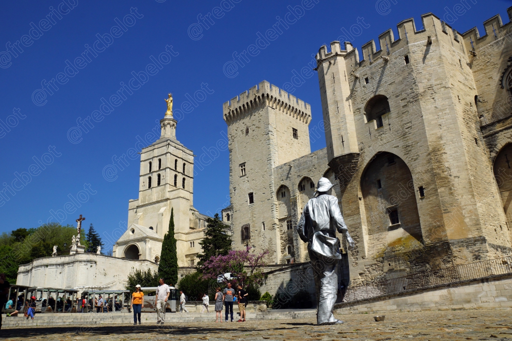 Les tours crénelées du Palais des Papes vues depuis une place animée de visiteurs.