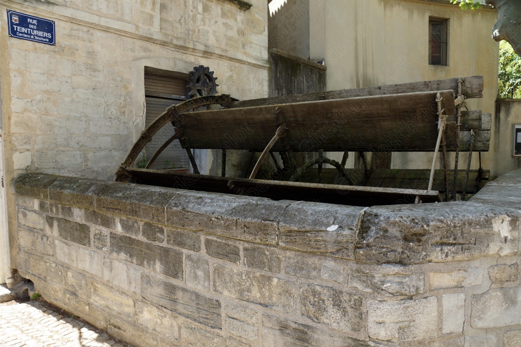 Un ancien mécanisme de moulin à eau en bois, installé le long d'un mur de pierre.