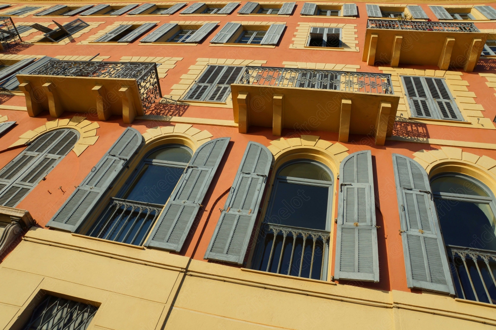 Façade colorée d'un immeuble niçois, avec ses volets et balcons en fer forgé.