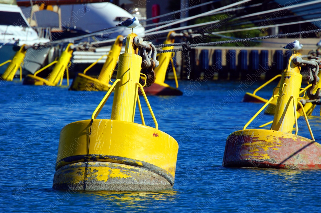 Des bouées d'amarrage jaunes flottent dans les eaux calmes d'un port.