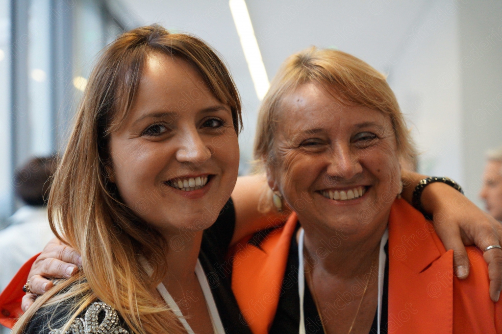 Deux femmes souriantes posent enlacées, badges de la convention autour du cou.