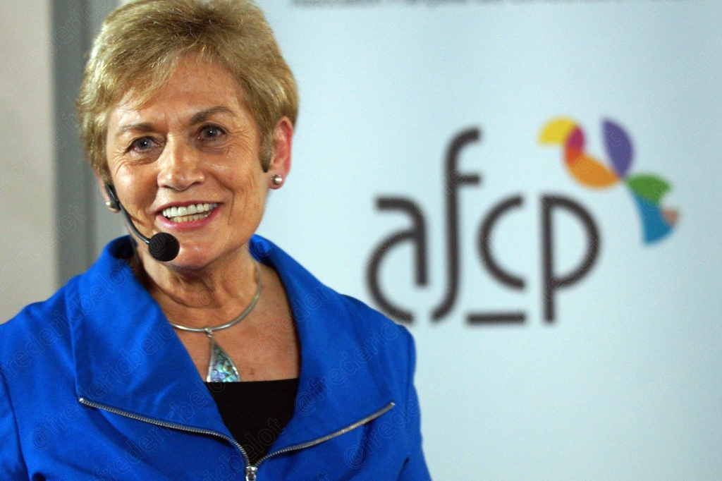 Une femme en veste bleue s'exprime au micro-cravate devant le logo AFCP.