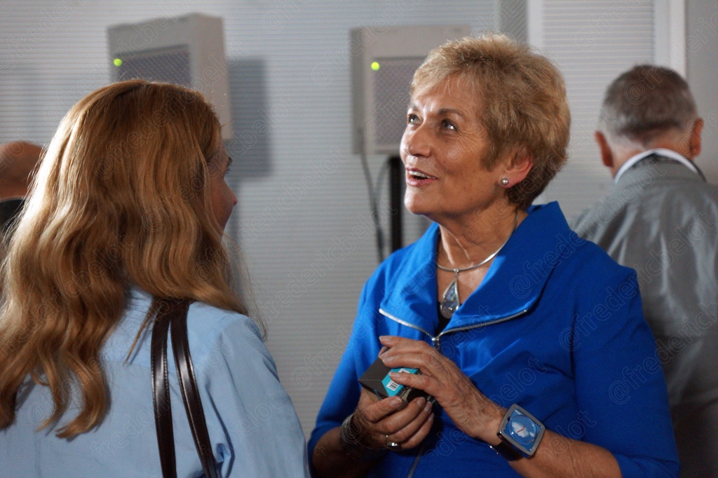 L'intervenante en bleu échange avec une autre femme aux cheveux blonds, en coulisses.
