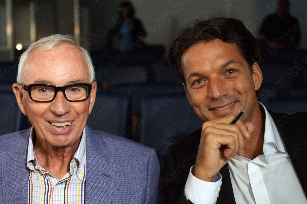 Un homme âgé et un homme plus jeune posent ensemble, souriants, devant le logo AFCP.