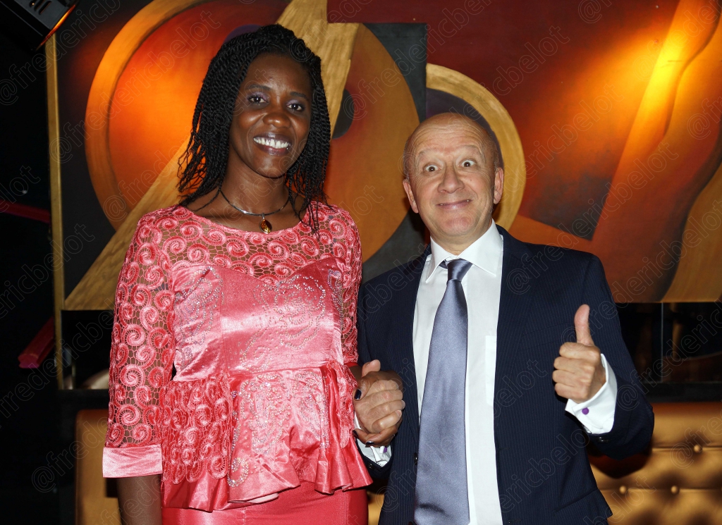 Une femme en robe rose et un homme en costume lèvent le pouce, souriants.