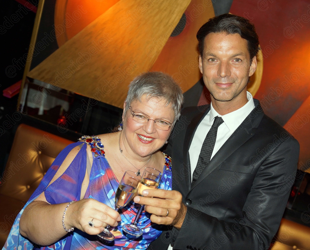 Une femme en robe bleue et un homme en costume posent devant le photo call.
