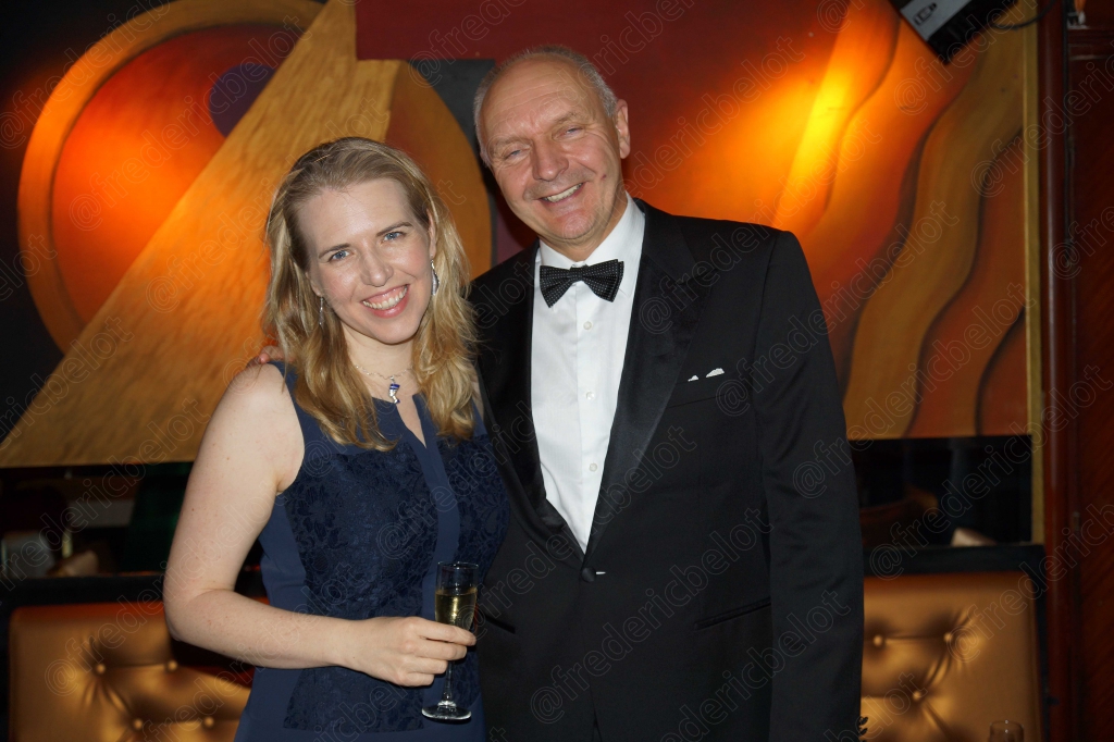 Une femme en robe bleu marine et un homme en smoking posent, souriants.