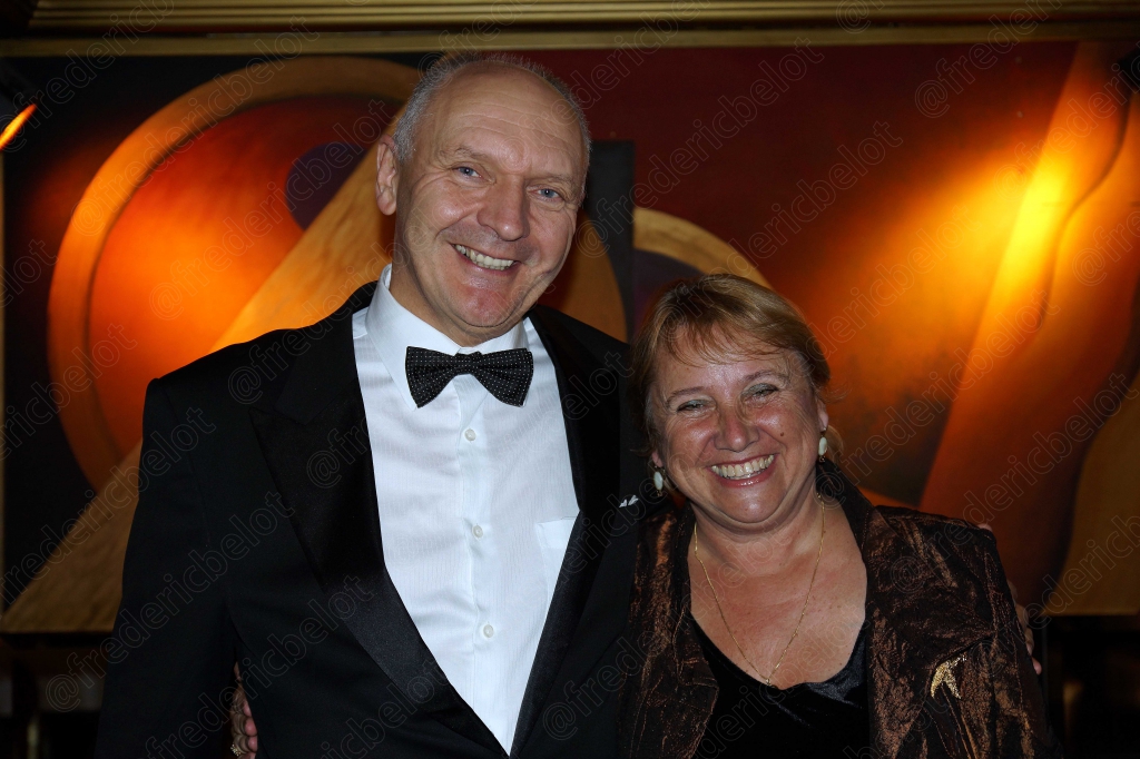 Un homme en nœud papillon et une femme en robe posent ensemble, souriants.