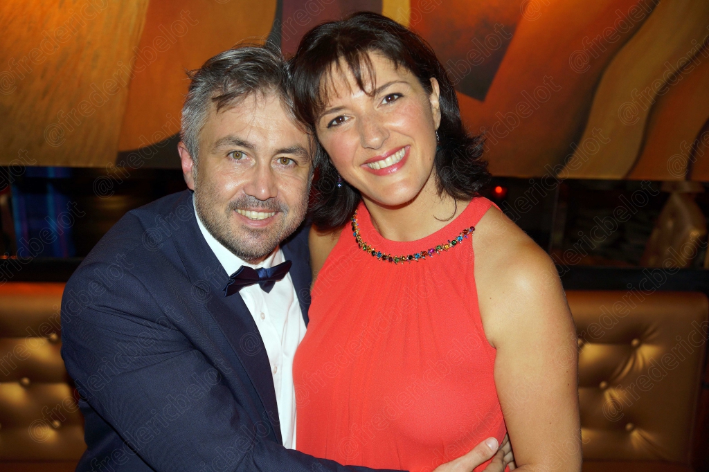 Un homme en smoking et une femme en robe corail posent, souriants.