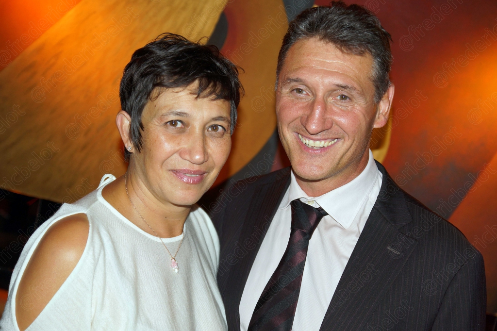 Une femme aux épaules dénudées et un homme en costume posent, souriants.