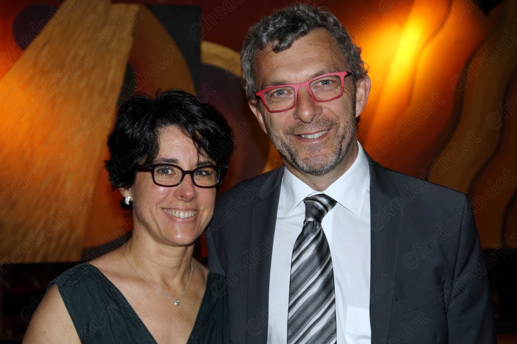 Une femme en robe sombre et lunettes rouges pose avec un homme en costume.
