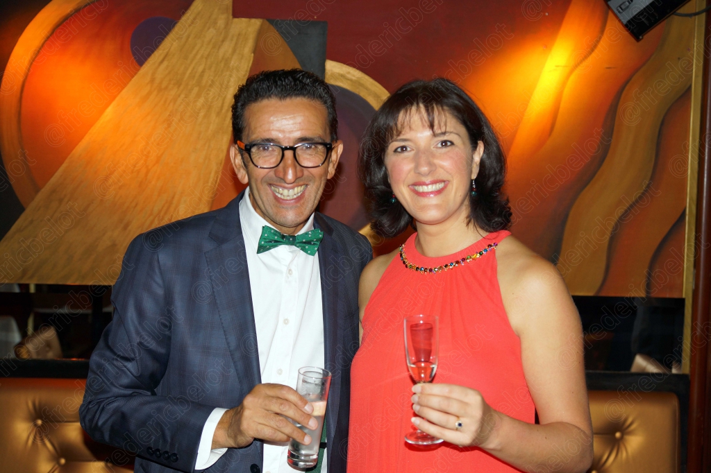 Un homme au nœud papillon vert et une femme en robe corail trinquent ensemble.
