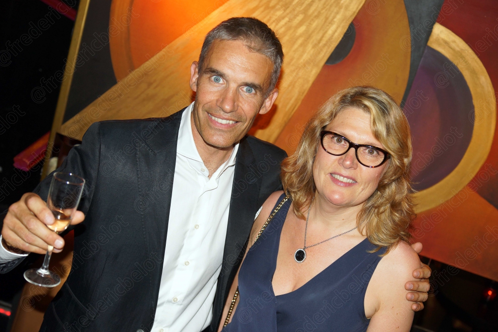 Un homme en costume et une femme à lunettes trinquent, coupes de champagne en main.