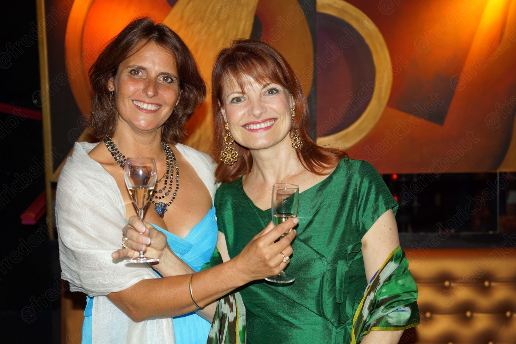 Deux femmes en robe verte et blanche trinquent, souriantes.