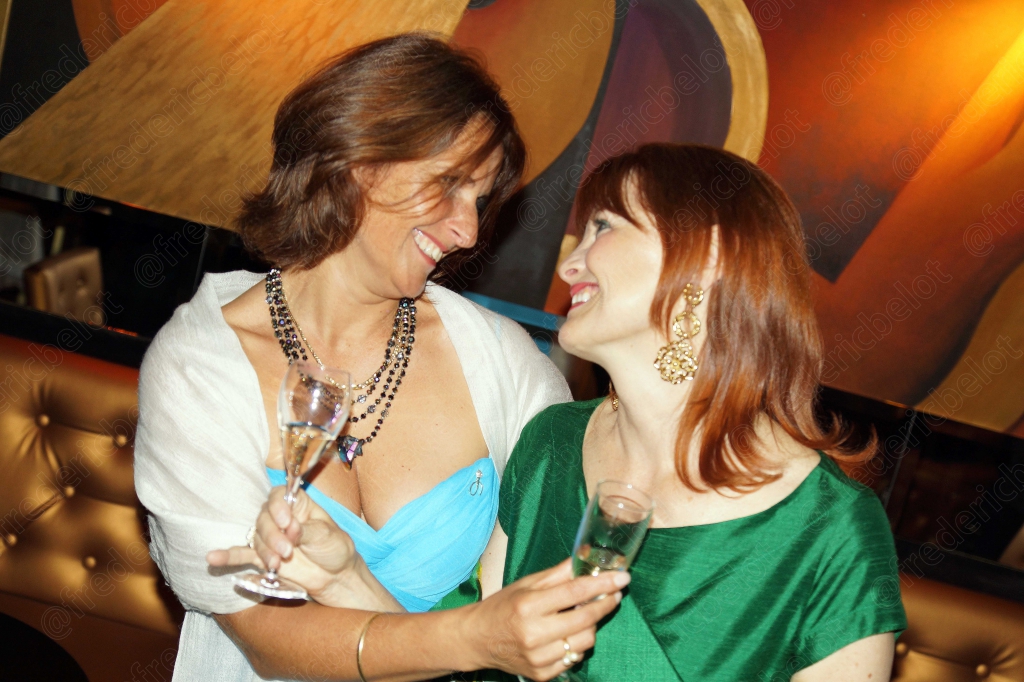 Deux femmes en robe verte et blanche partagent un moment complice.