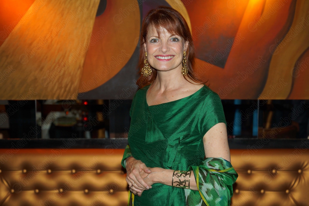 Portrait souriant d'une femme en robe verte, bras croisés.