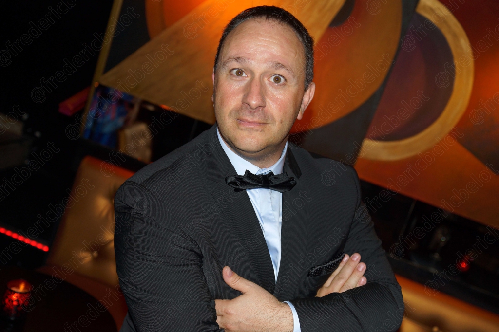 Portrait d'un homme en costume sombre, bras croisés, devant le photo call.