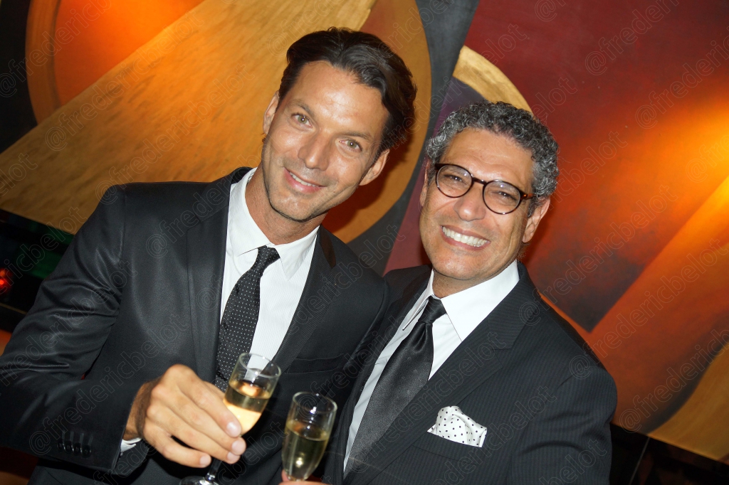 Un homme en costume et un homme en smoking trinquent, souriants.