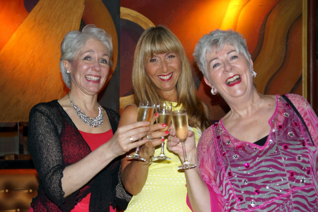 Trois femmes en robe de soirée trinquent ensemble, souriantes.