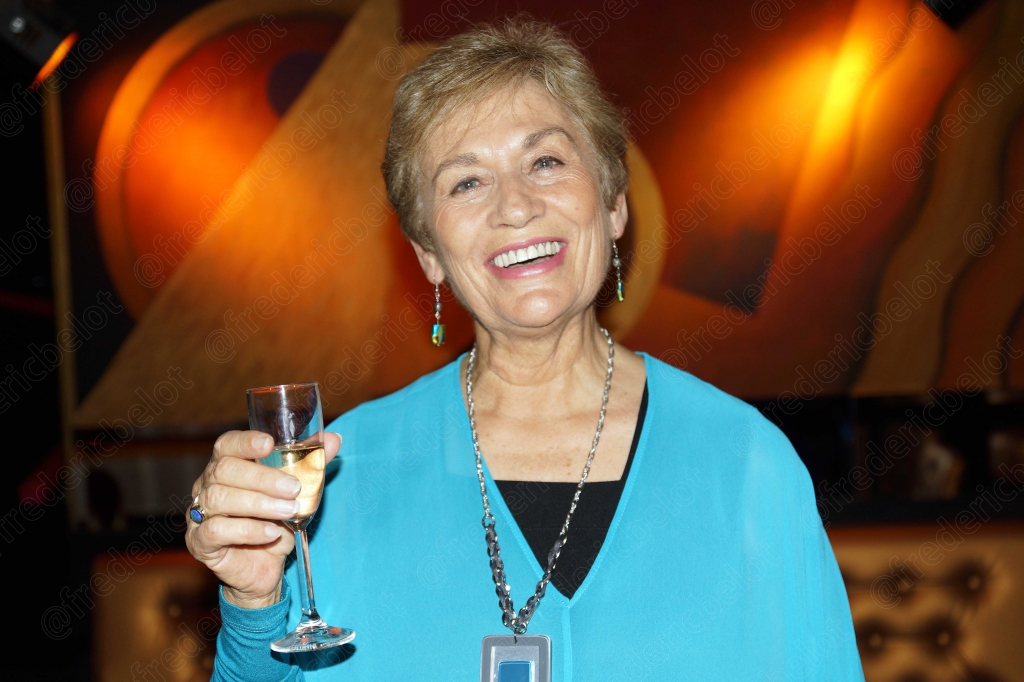 Portrait souriant d'une femme aux cheveux blancs, coupe de champagne à la main.