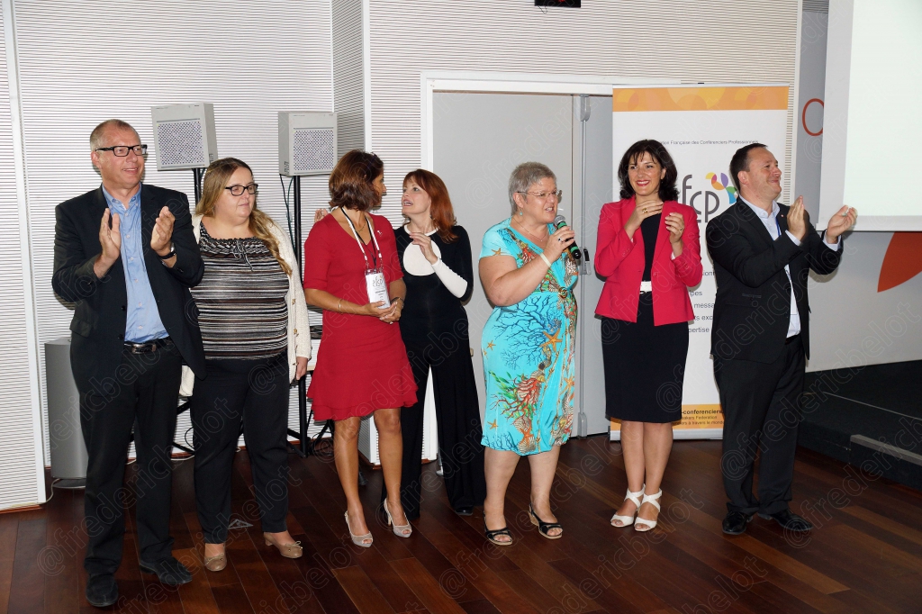 Le même groupe applaudit, souriant, devant les portes vitrées de la salle.
