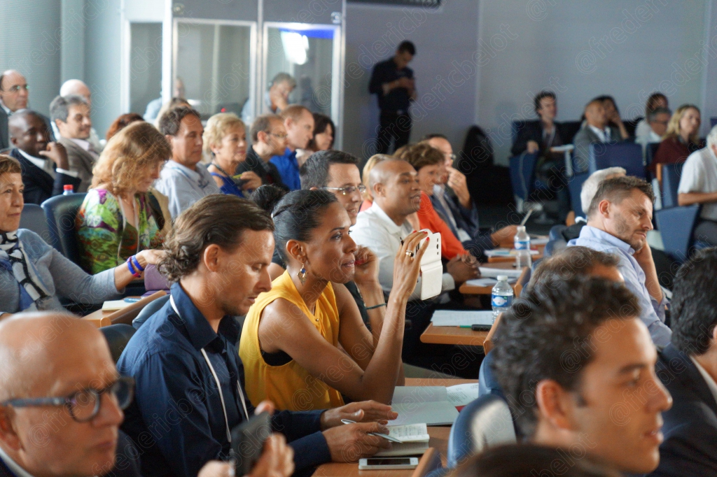 Le public assis en rangées suit la conférence, ordinateurs portables ouverts.