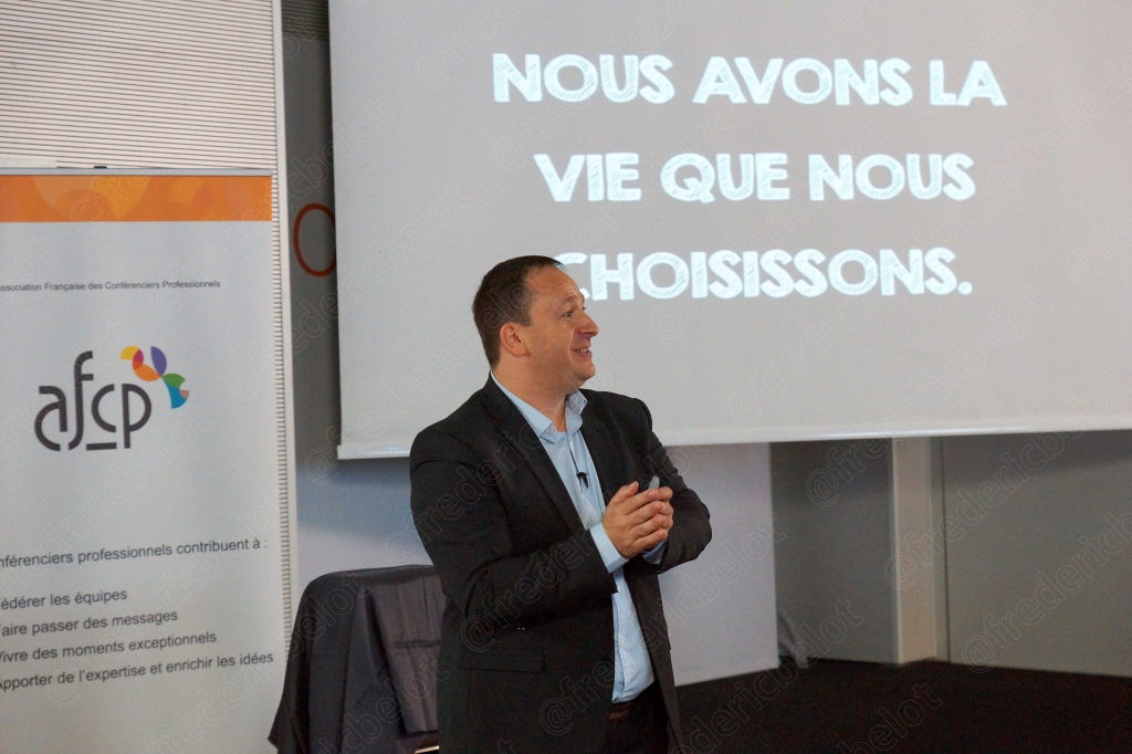 Homme en costume devant un écran affichant « Nous avons la vie que nous choisissons »