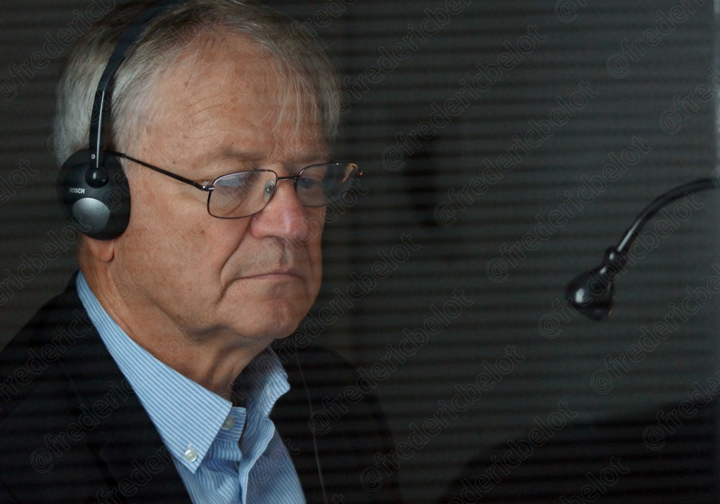 Homme aux cheveux gris portant un casque-micro de radio, expression concentrée